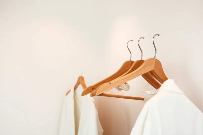 Kunststoff kleiderbügel elegant drapiert auf einem Holzkleiderständer im sanften Licht.